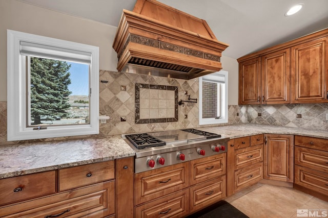 2501 Kensington Pl, Carson City, NV 89703 - kitchen with custom exhaust hood, stainless steel gas cooktop, brown cabinets, decorative backsplash, and light stone counters