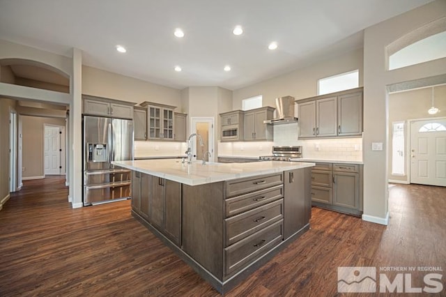 kitchen with stainless steel fridge with ice dispenser, wall chimney exhaust hood, dark wood-style flooring, decorative backsplash, and glass insert cabinets