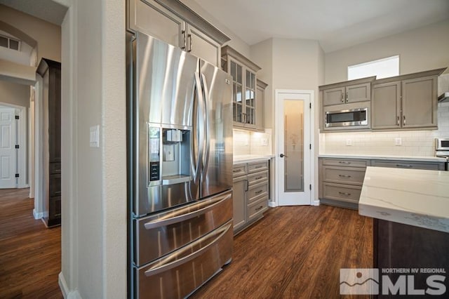 kitchen featuring appliances with stainless steel finishes, backsplash, gray cabinetry, and dark wood-style floors
