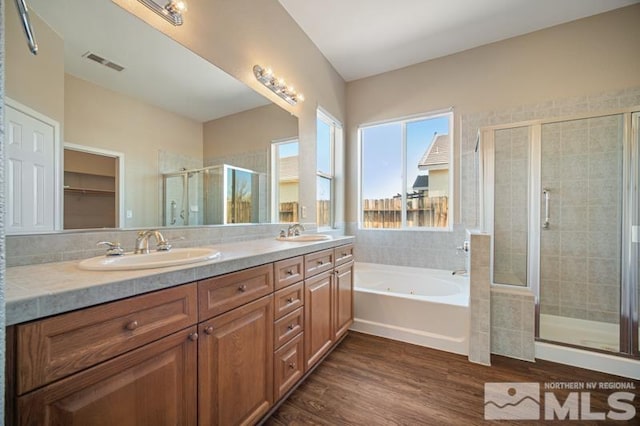 full bath featuring a shower stall, a tub with jets, double vanity, and wood finished floors
