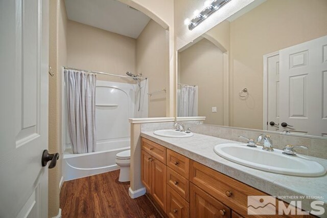 full bathroom with wood finished floors, double vanity, shower / tub combo, and toilet