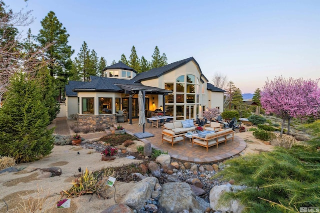 120 W Willis Ln, Reno, NV 89511 - back of house at dusk with a patio area, an outdoor living space, stucco siding, and roof with shingles