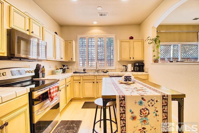 2078 Tivoli, Sparks, NV 89434 - kitchen with appliances with stainless steel finishes, tile countertops, a sink, arched walkways, and light wood-style floors