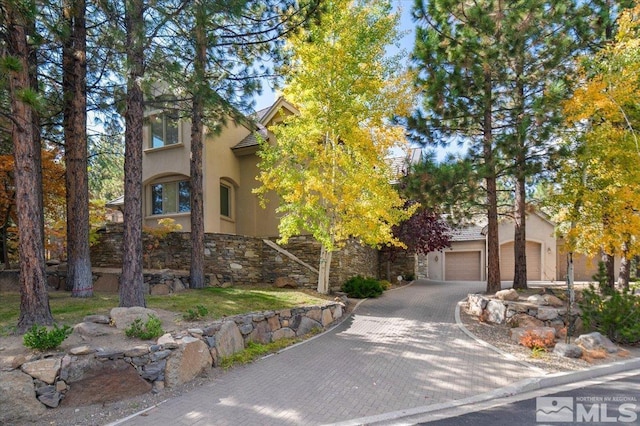 5680 Lausanne Dr, Reno, NV 89511 - view of property hidden behind natural elements with stucco siding, stone siding, decorative driveway, and a garage