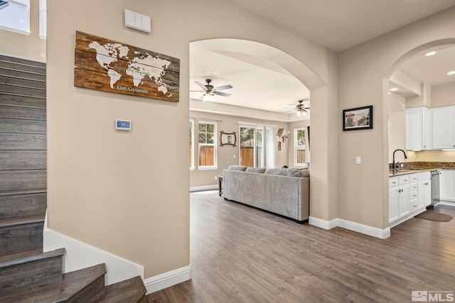 corridor featuring stairs, dark wood-style flooring, baseboards, arched walkways, and a sink