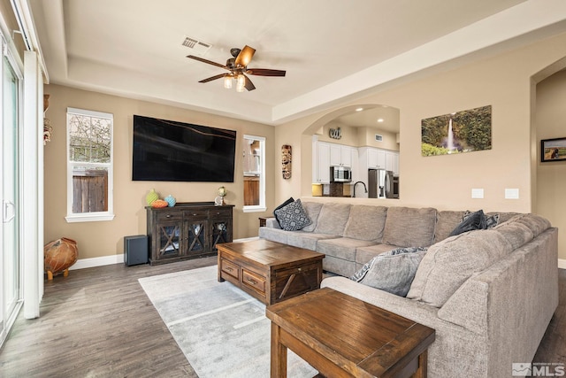 living area with wood finished floors, a ceiling fan, baseboards, arched walkways, and a raised ceiling