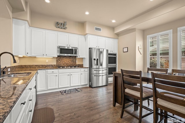 kitchen with stainless steel appliances, a sink, dark wood-style flooring, recessed lighting, and dark stone counters