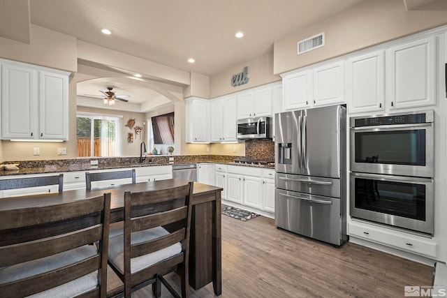 kitchen featuring appliances with stainless steel finishes, wood finished floors, white cabinetry, arched walkways, and recessed lighting