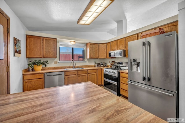 11000 Bighorn Dr, Reno, NV 89508 - kitchen featuring appliances with stainless steel finishes, a sink, vaulted ceiling, brown cabinets, and a textured ceiling