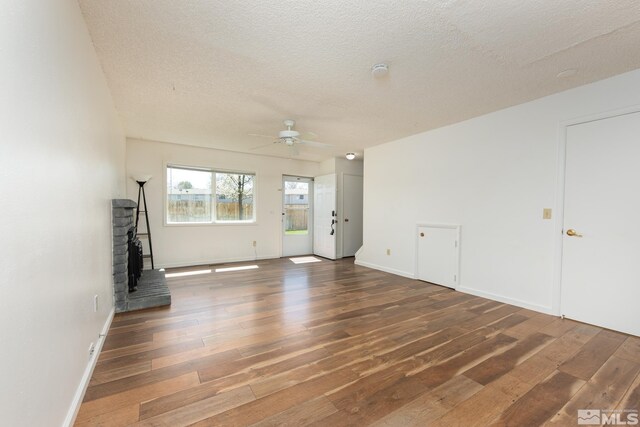unfurnished living room with hardwood / wood-style flooring, ceiling fan, a wood stove, a textured ceiling, and baseboards