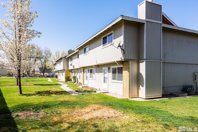 back of property with a lawn, a chimney, brick siding, and a residential view