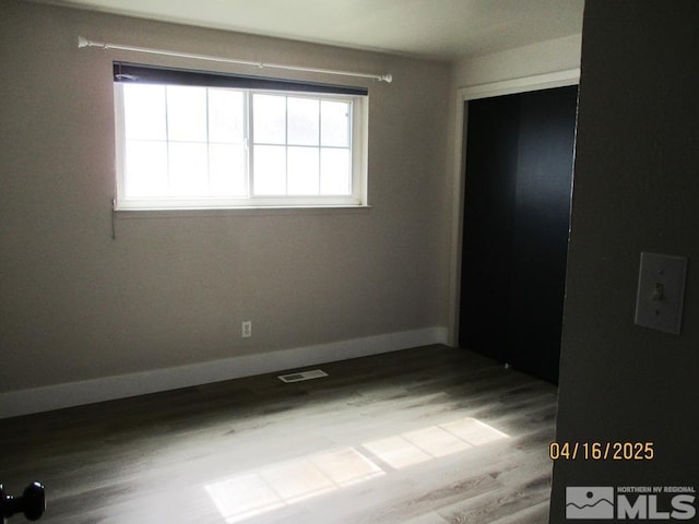 unfurnished bedroom with wood finished floors, baseboards, and a closet