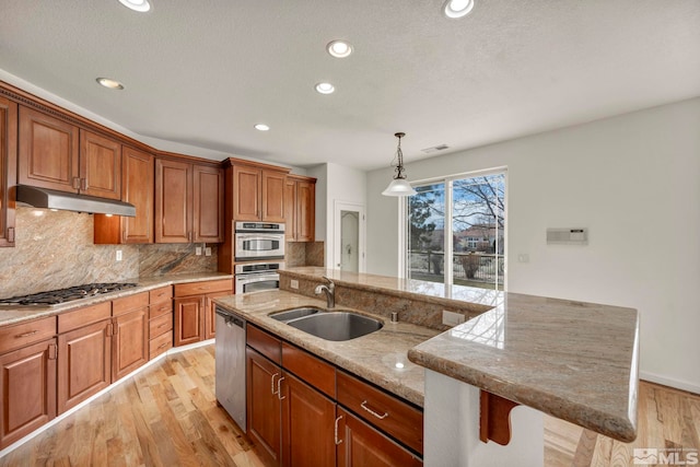 6647 Fabric Dr, Sparks, NV 89436 - kitchen featuring a sink, under cabinet range hood, appliances with stainless steel finishes, light wood-style flooring, and brown cabinetry