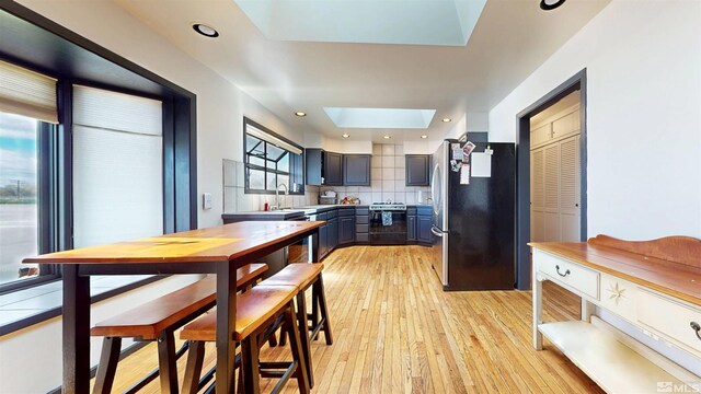 kitchen featuring freestanding refrigerator, a skylight, range with electric stovetop, light countertops, and light wood-style floors