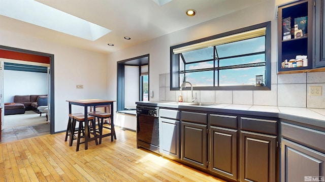 kitchen with black dishwasher, a skylight, a sink, light wood-type flooring, and dark brown cabinets