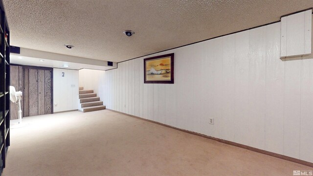 finished below grade area featuring carpet floors, stairs, a textured ceiling, and baseboards