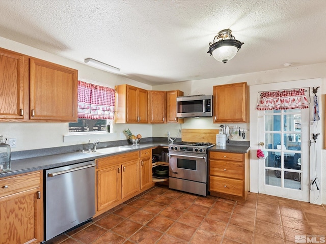 325 Stock Ln, Fernley, NV 89408 - kitchen with appliances with stainless steel finishes, a sink, dark countertops, a textured ceiling, and brown cabinetry