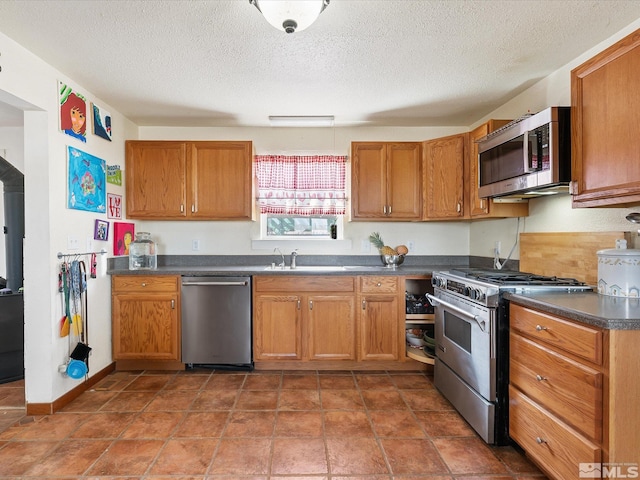325 Stock Ln, Fernley, NV 89408 - kitchen with appliances with stainless steel finishes, dark countertops, a textured ceiling, brown cabinets, and a sink