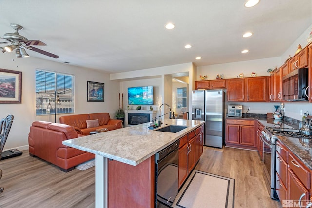 kitchen featuring stainless steel appliances, a sink, recessed lighting, open floor plan, and light wood finished floors