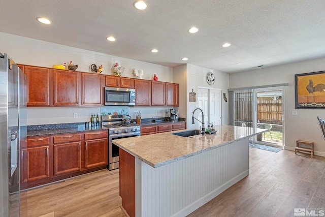 kitchen featuring stainless steel appliances, a sink, light wood-type flooring, recessed lighting, and a kitchen island with sink