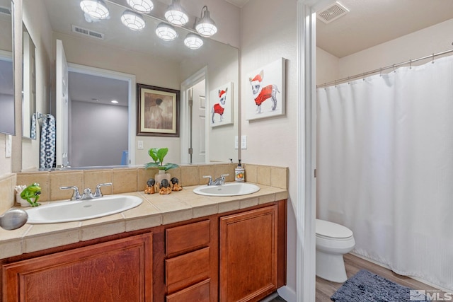 bathroom featuring wood finished floors, toilet, double vanity, and curtained shower