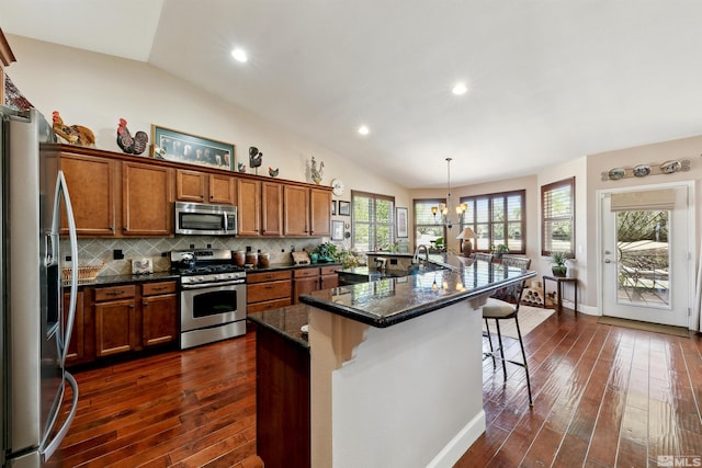 1367 Porter Dr, Minden, NV 89423 - kitchen featuring stainless steel appliances, vaulted ceiling, brown cabinets, dark wood-style floors, and a kitchen bar