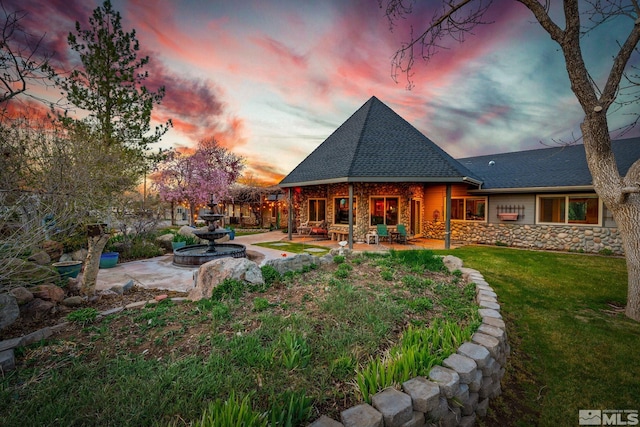 951 Riverview Dr, Gardnerville, NV 89460 - back of house at dusk with a patio, stone siding, roof with shingles, and a lawn