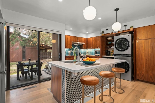 kitchen with stacked washer / dryer, brown cabinetry, light countertops, light wood finished floors, and a sink