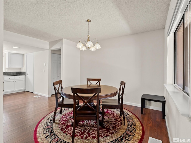 dining area with a chandelier, wood finished floors, a textured ceiling, and baseboards