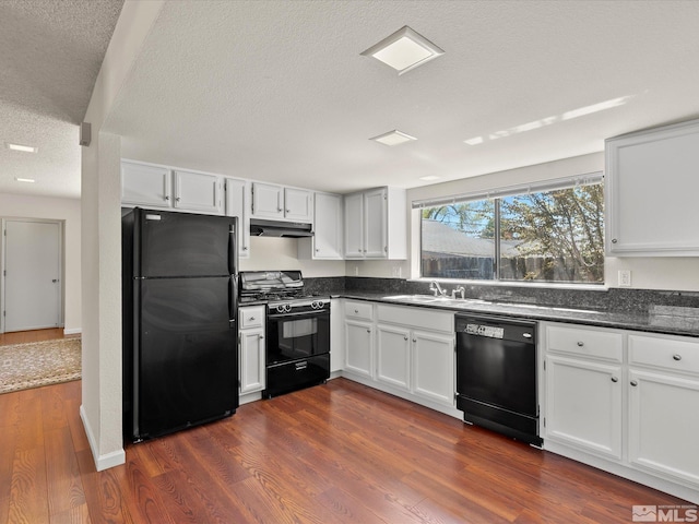 kitchen with black appliances, under cabinet range hood, dark countertops, dark wood-style floors, and a textured ceiling