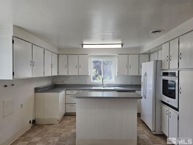 311 S Main St, Yerington, NV 89447 - kitchen with oven, white refrigerator with ice dispenser, a sink, a kitchen island, and white cabinetry