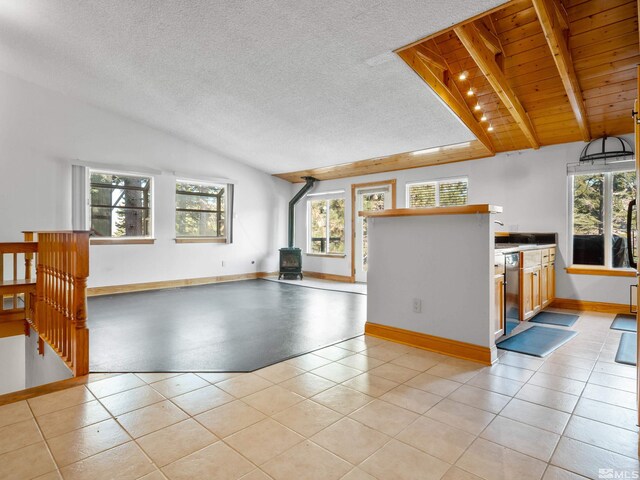unfurnished living room with a wood stove, plenty of natural light, lofted ceiling, baseboards, and a textured ceiling