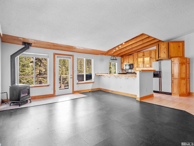 unfurnished living room with a textured ceiling, a wood stove, vaulted ceiling, and baseboards