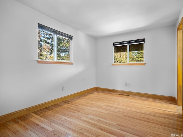 empty room featuring plenty of natural light, light wood finished floors, and baseboards