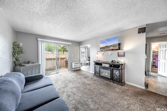 carpeted living area with a wall mounted air conditioner, a textured ceiling, baseboards, and a glass covered fireplace
