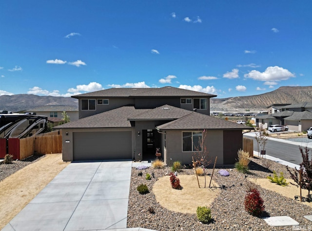 prairie-style home featuring a mountain view, driveway, fence, an attached garage, and stucco siding