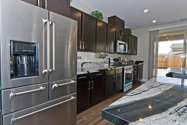 kitchen featuring appliances with stainless steel finishes, dark wood finished floors, light stone counters, dark brown cabinets, and recessed lighting