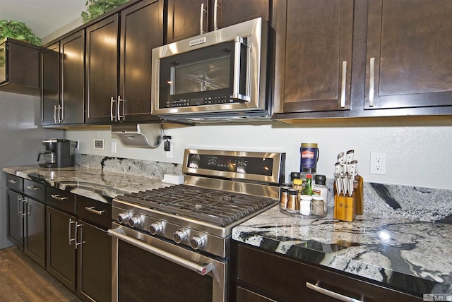 kitchen with appliances with stainless steel finishes, light stone countertops, dark brown cabinets, and dark wood-style flooring