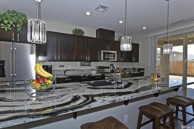 kitchen featuring stainless steel appliances, a chandelier, a kitchen bar, light stone counters, and recessed lighting