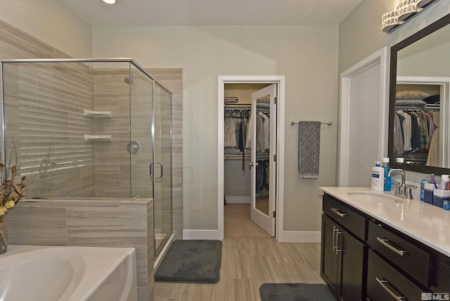 bathroom featuring a stall shower, vanity, a bath, baseboards, and a spacious closet