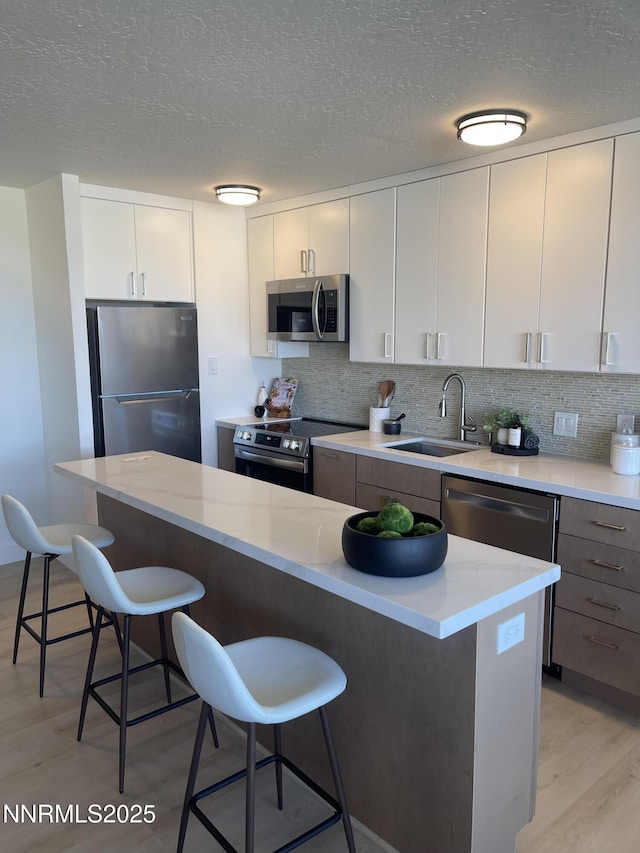 100 N Arlington Ave # 6G, Reno, NV 89501 - kitchen featuring appliances with stainless steel finishes, light wood finished floors, a kitchen breakfast bar, decorative backsplash, and white cabinets