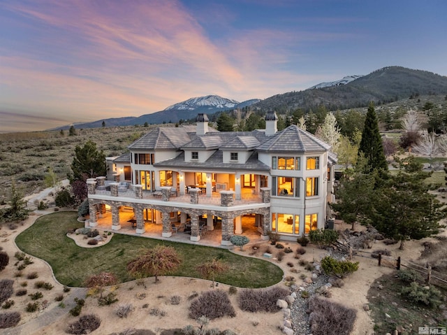 12360 High Vista Dr, Reno, NV 89511 - back of house at dusk with a patio area, a chimney, a balcony, a lawn, and a mountain view