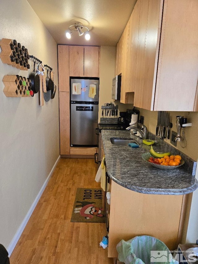 kitchen with stainless steel appliances, a sink, light wood-style floors, baseboards, and light brown cabinets
