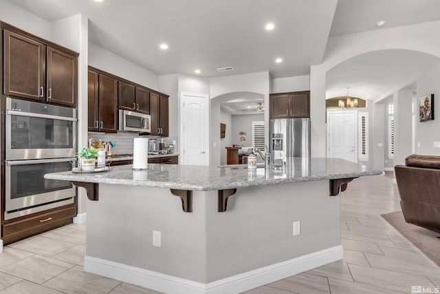11641 Diamond Stream Dr, Sparks, NV 89441 - kitchen featuring appliances with stainless steel finishes, arched walkways, a kitchen bar, dark brown cabinets, and a chandelier