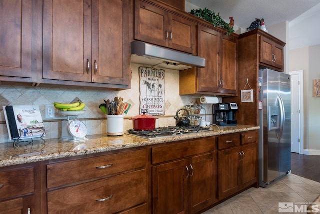 1058 Aspen Brook Ln, Gardnerville, NV 89460 - kitchen with appliances with stainless steel finishes, under cabinet range hood, light stone counters, tasteful backsplash, and light tile patterned floors