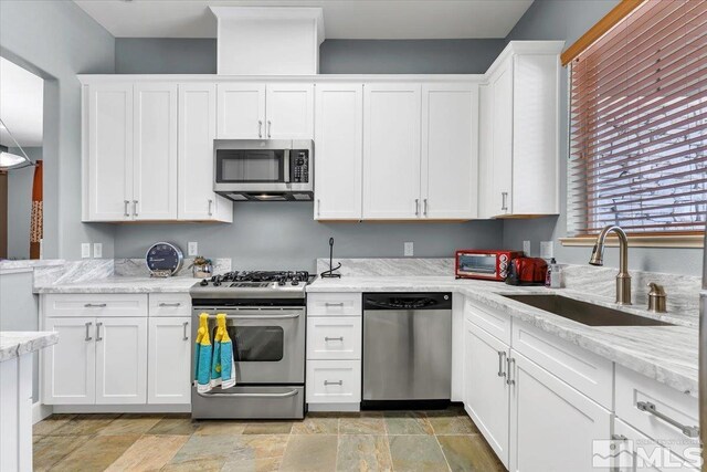4889 Bougainvillea Cir, Sparks, NV 89436 - kitchen with stainless steel appliances, a sink, white cabinetry, light stone finish flooring, and light stone countertops