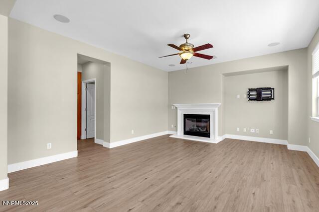 1095 S University Park Loop, Reno, NV 89512 - unfurnished living room with ceiling fan, wood finished floors, a glass covered fireplace, and baseboards