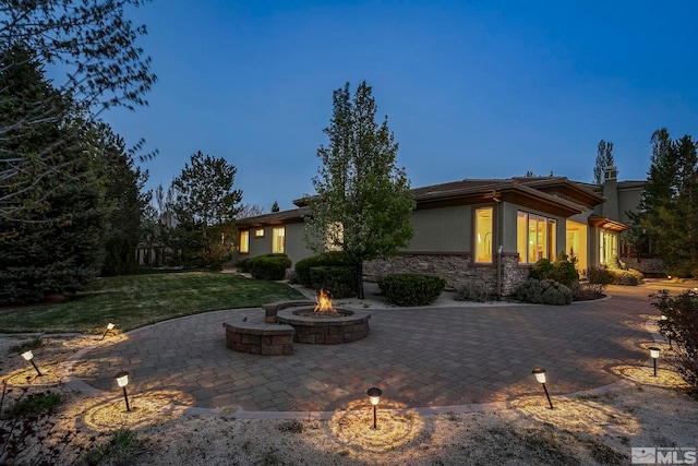 rear view of house with an outdoor fire pit, stucco siding, a patio area, a lawn, and stone siding