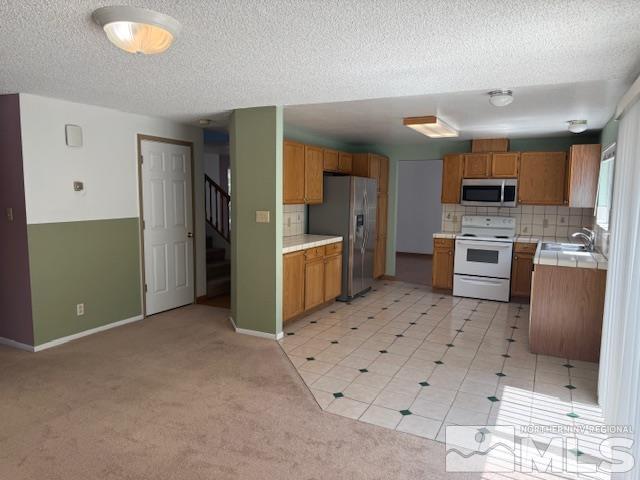 6700 Sandia Dr, Reno, NV 89523 - kitchen with appliances with stainless steel finishes, tile countertops, brown cabinetry, tasteful backsplash, and a textured ceiling