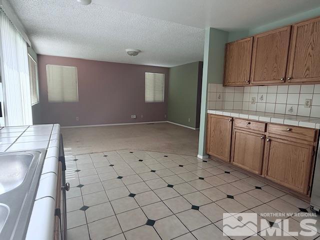 6700 Sandia Dr, Reno, NV 89523 - kitchen with tile countertops, light carpet, brown cabinetry, baseboards, and open floor plan